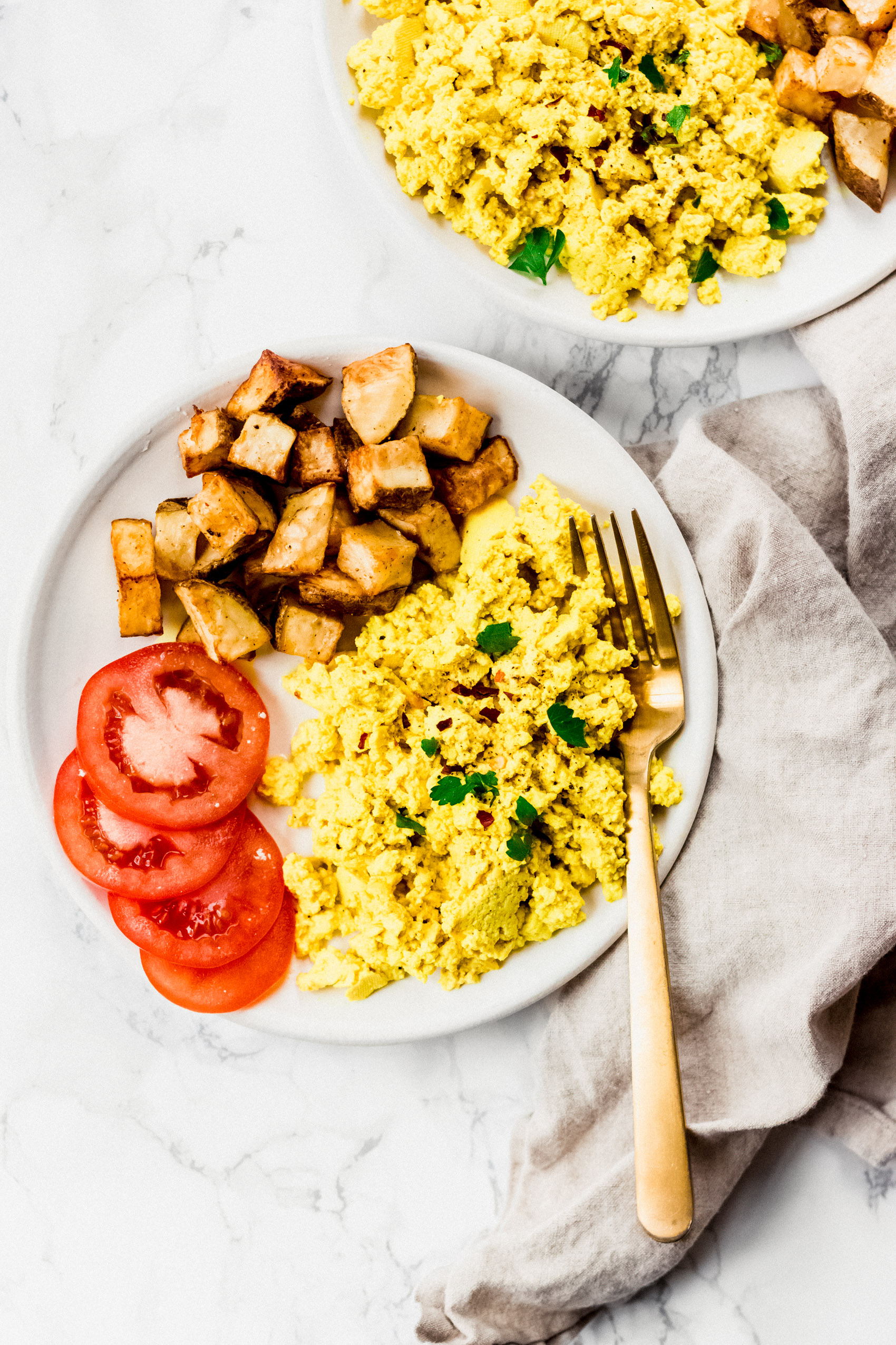 a plate of tofu scramble served with tomatoes and roasted breakfast potatoes