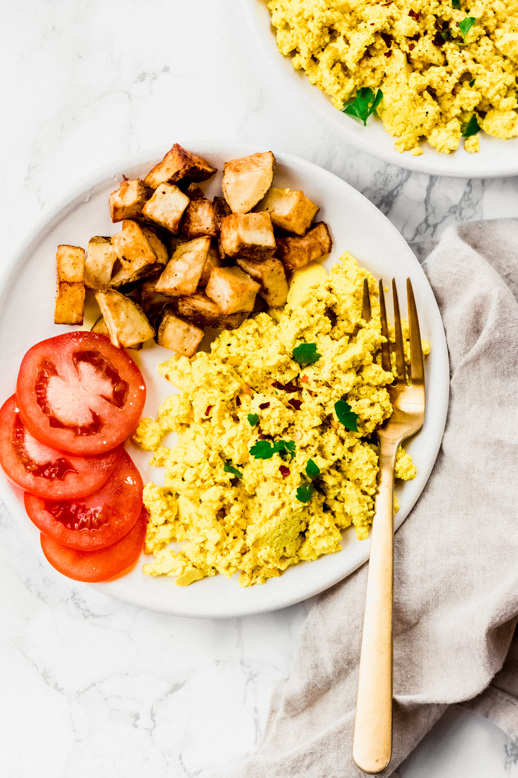 a plate of scrambled tofu served with fresh tomatoes and roasted potatoes