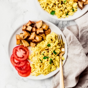 a plate of vegan tofu scramble served with roasted potatoes and fresh sliced tomatoes