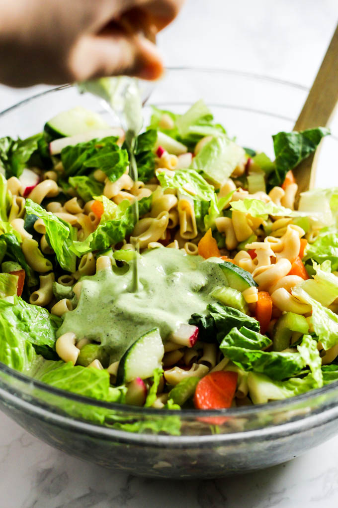a large bowl of salad being topped with a homemade vegan ranch dressing