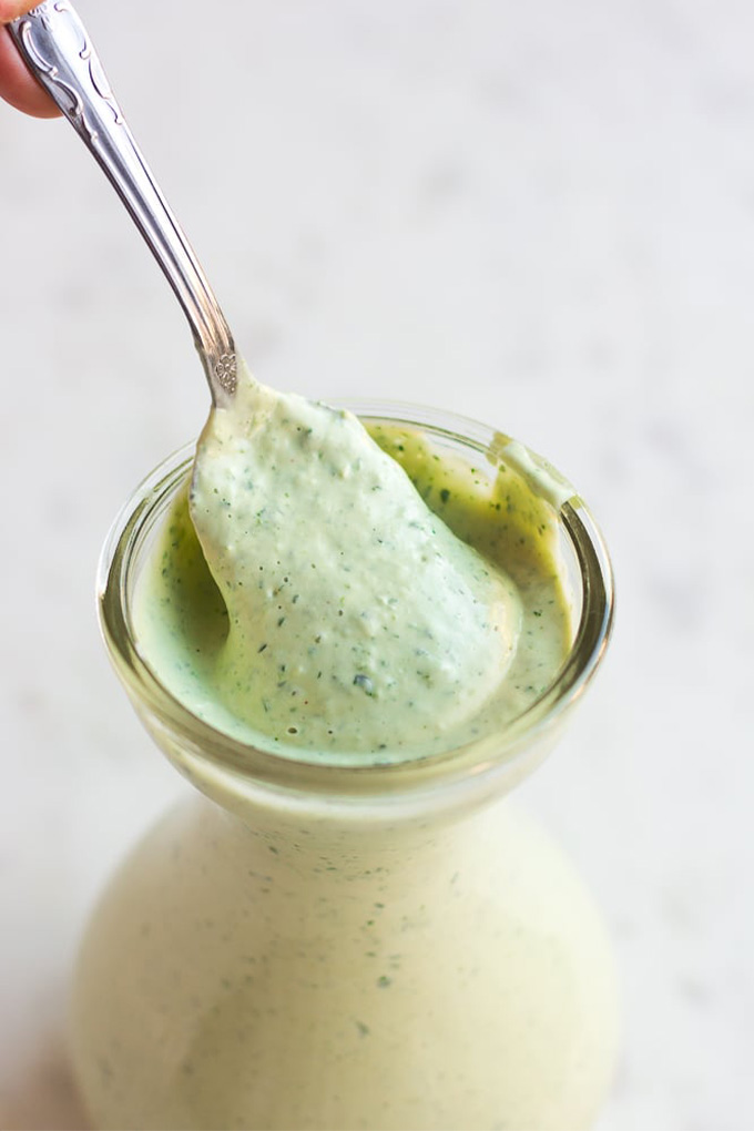 a jar of homemade vegan green goddess dressing being served with a spoon