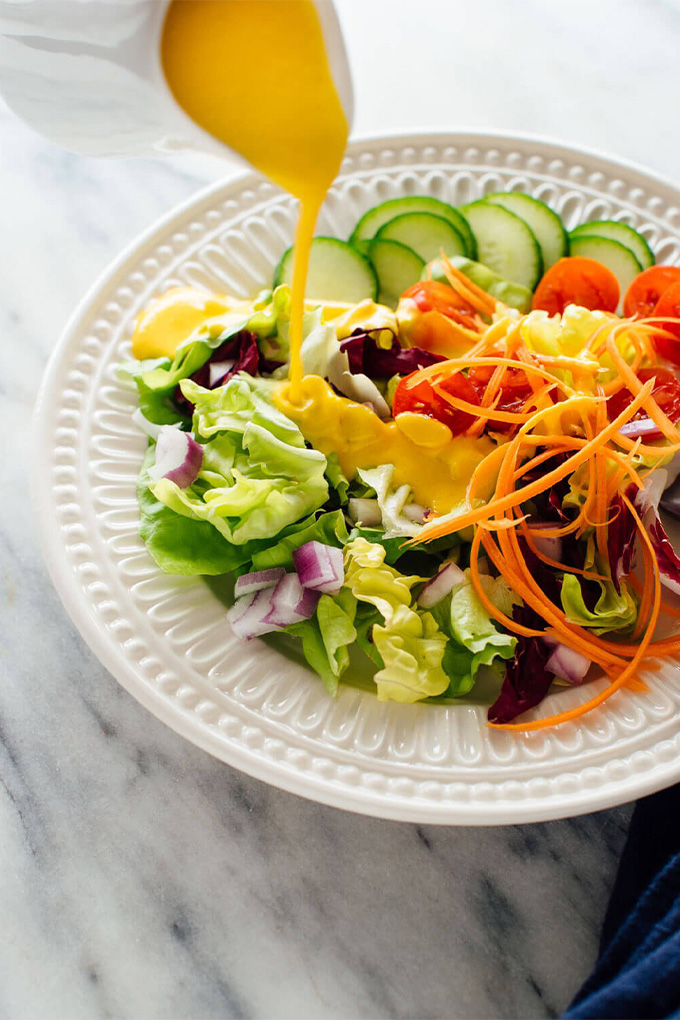a bowl of salad being topped with a carrot ginger dressing