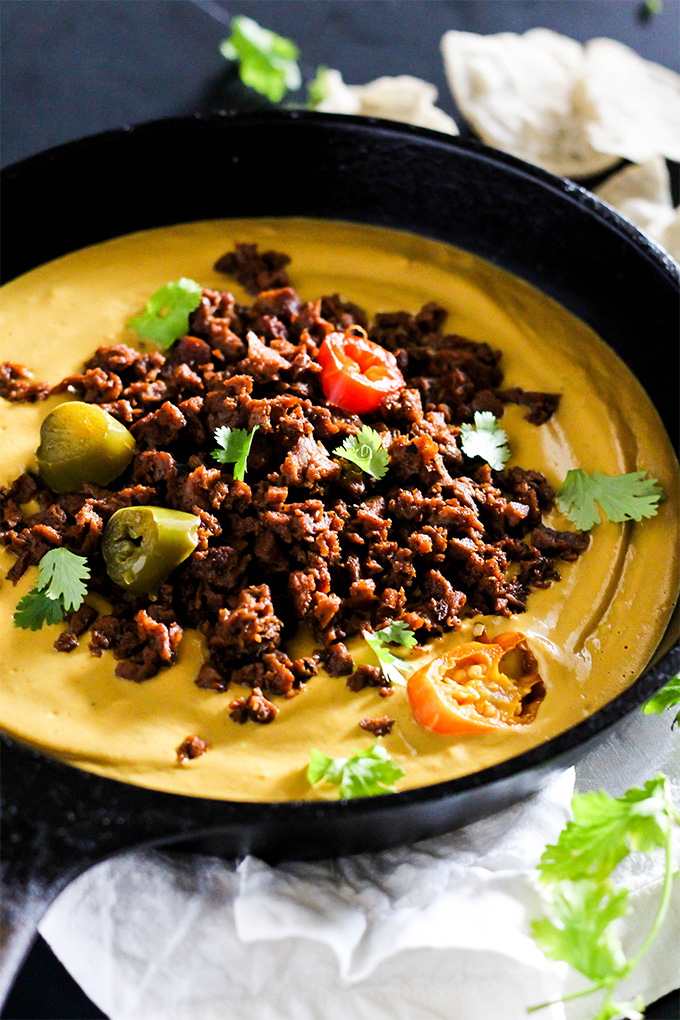 a cast iron skillet of vegan queso topped with chili, chopped peppers and cilantro