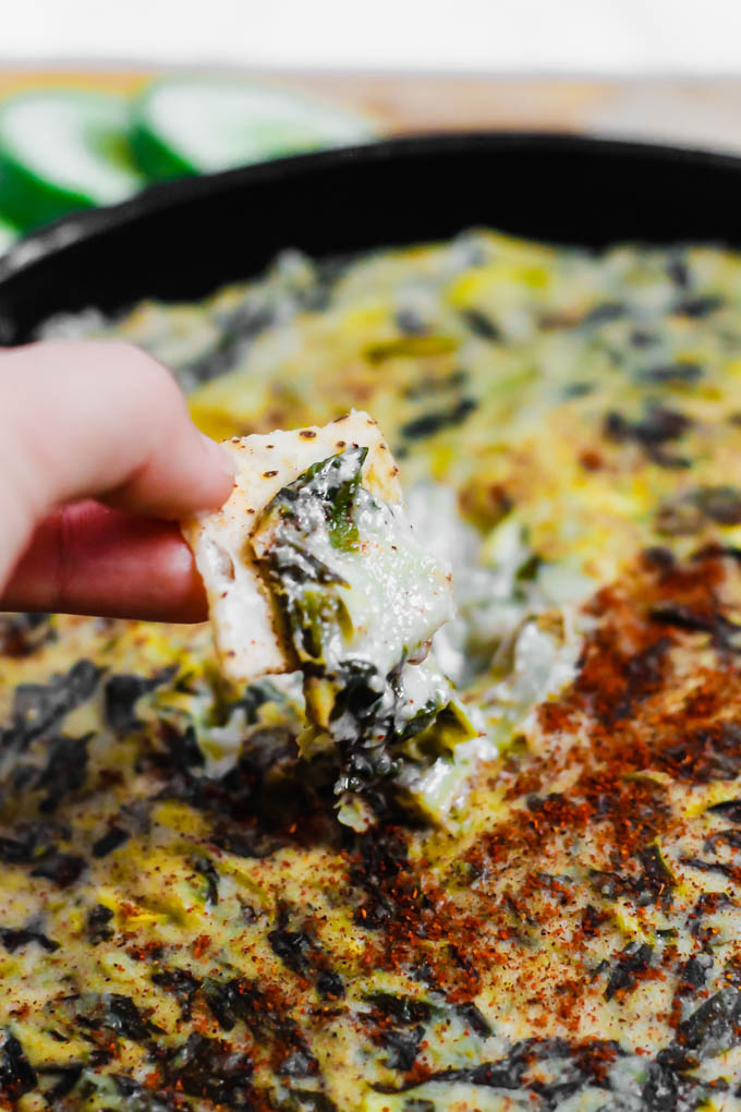 a chip being dipped into a skillet of vegan spinach artichoke dip