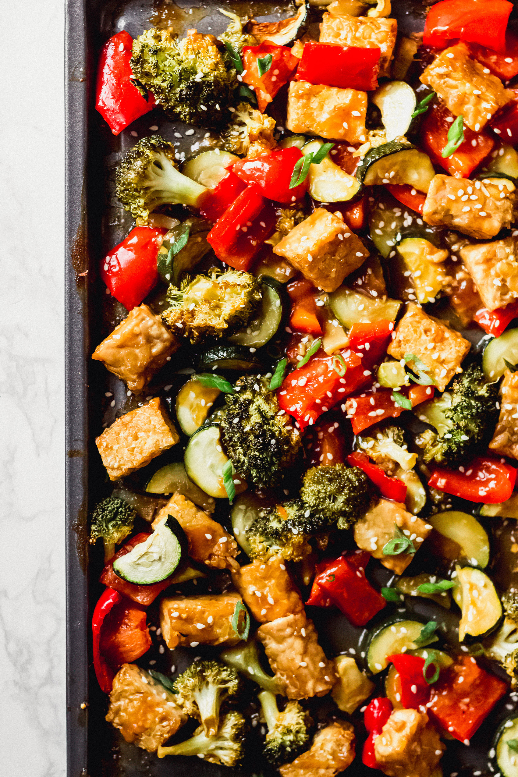 a sheet tray of chopped veggies and cubed tempeh topped with sesame seeds