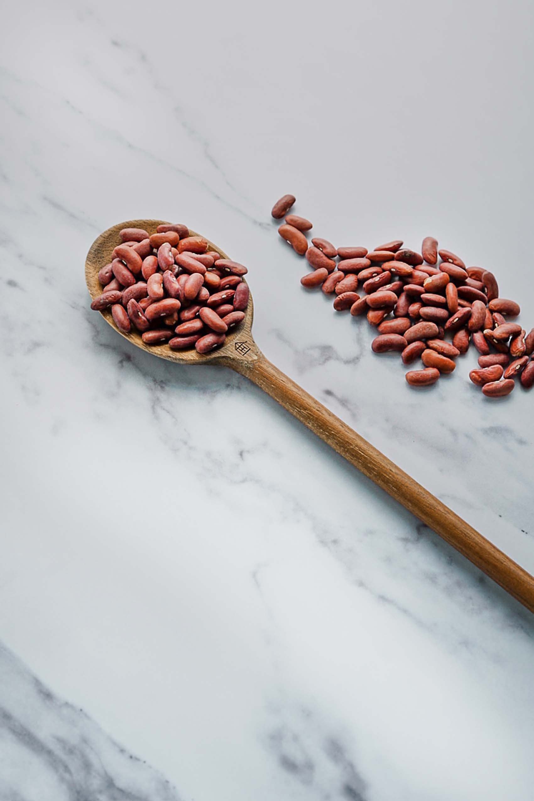 dried red beans scattered on a white marble countertop alongside a wooden spoon