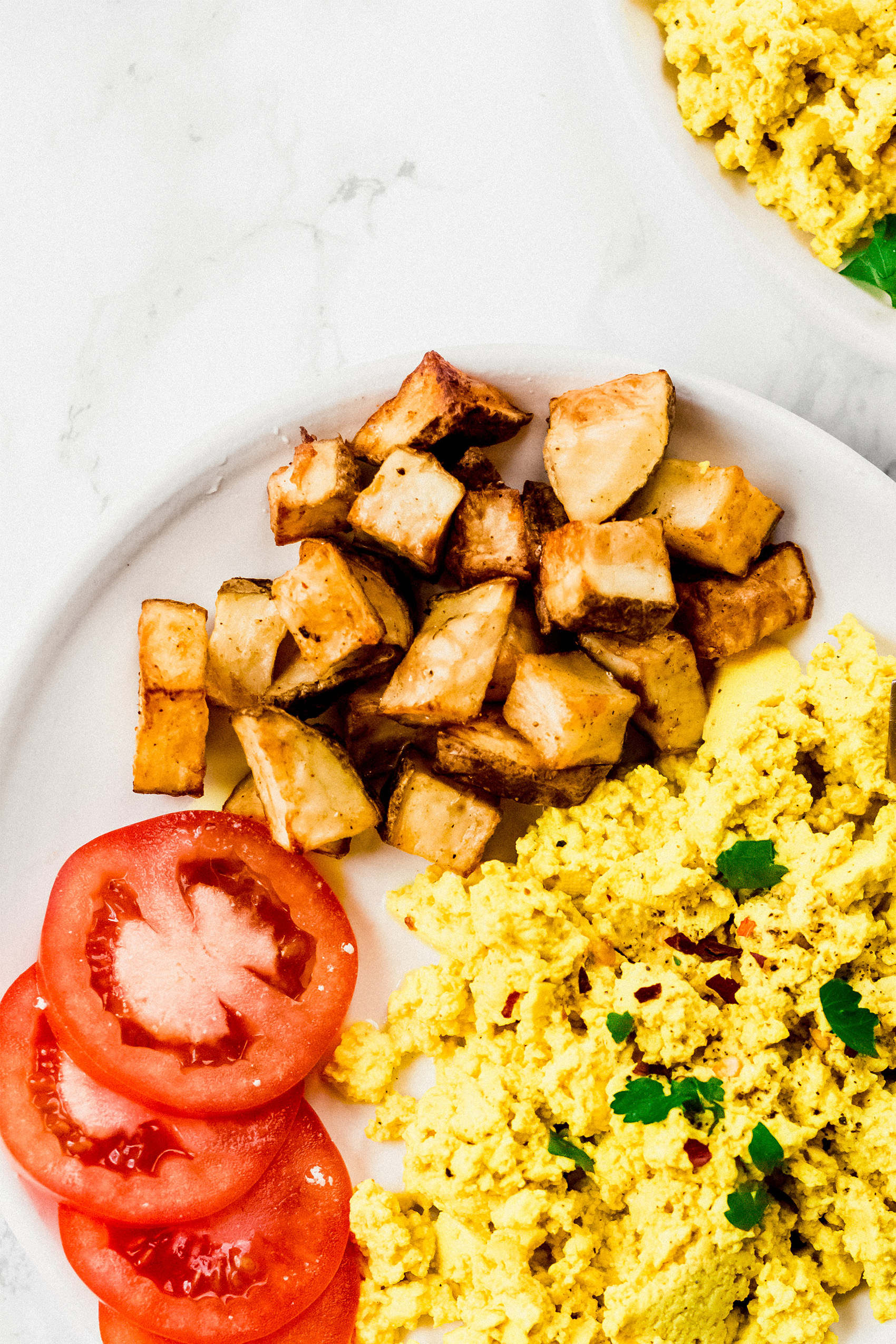 a plate of tofu scramble, roasted potatoes and sliced tomato