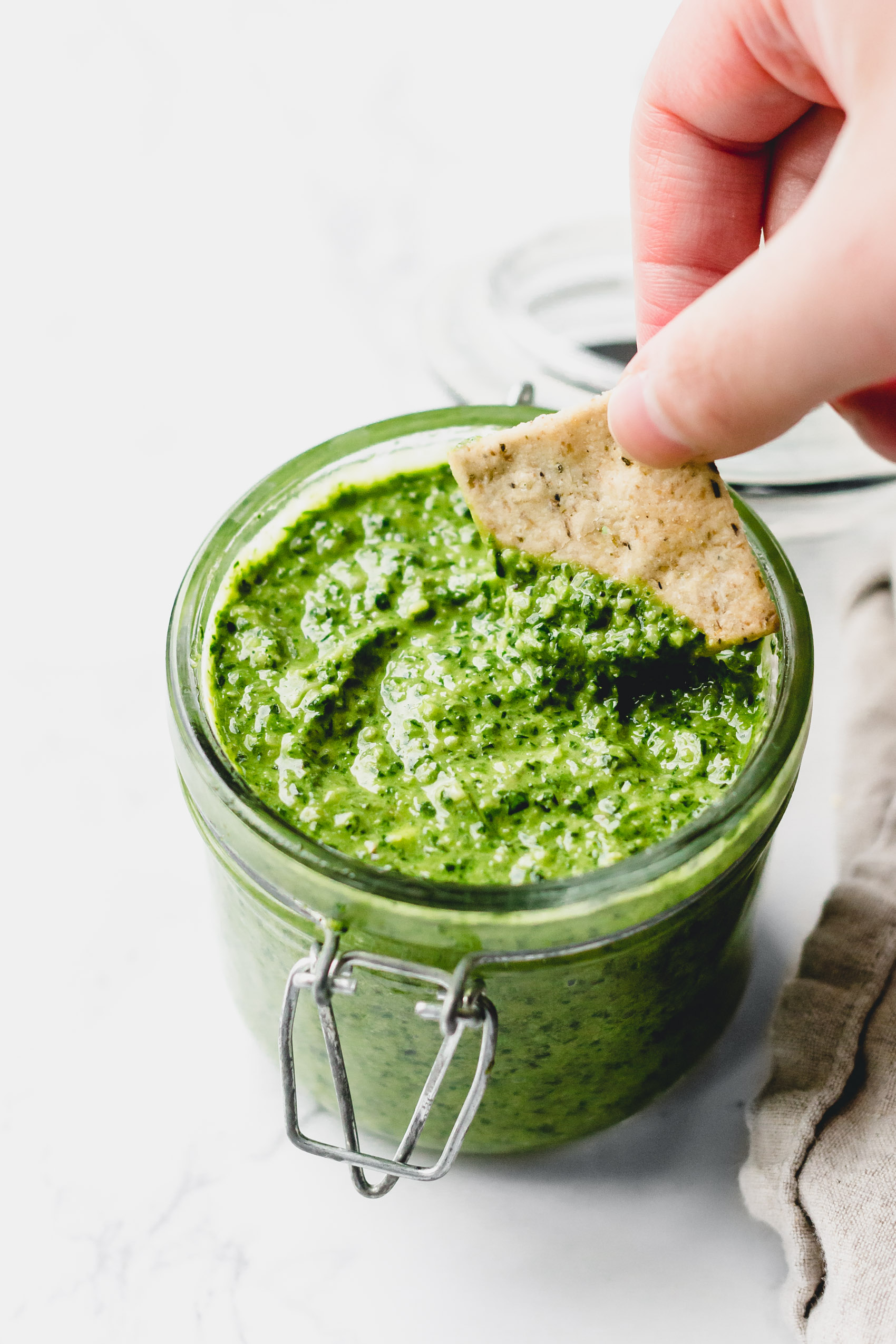 a cracker being dipped into a jar of pesto