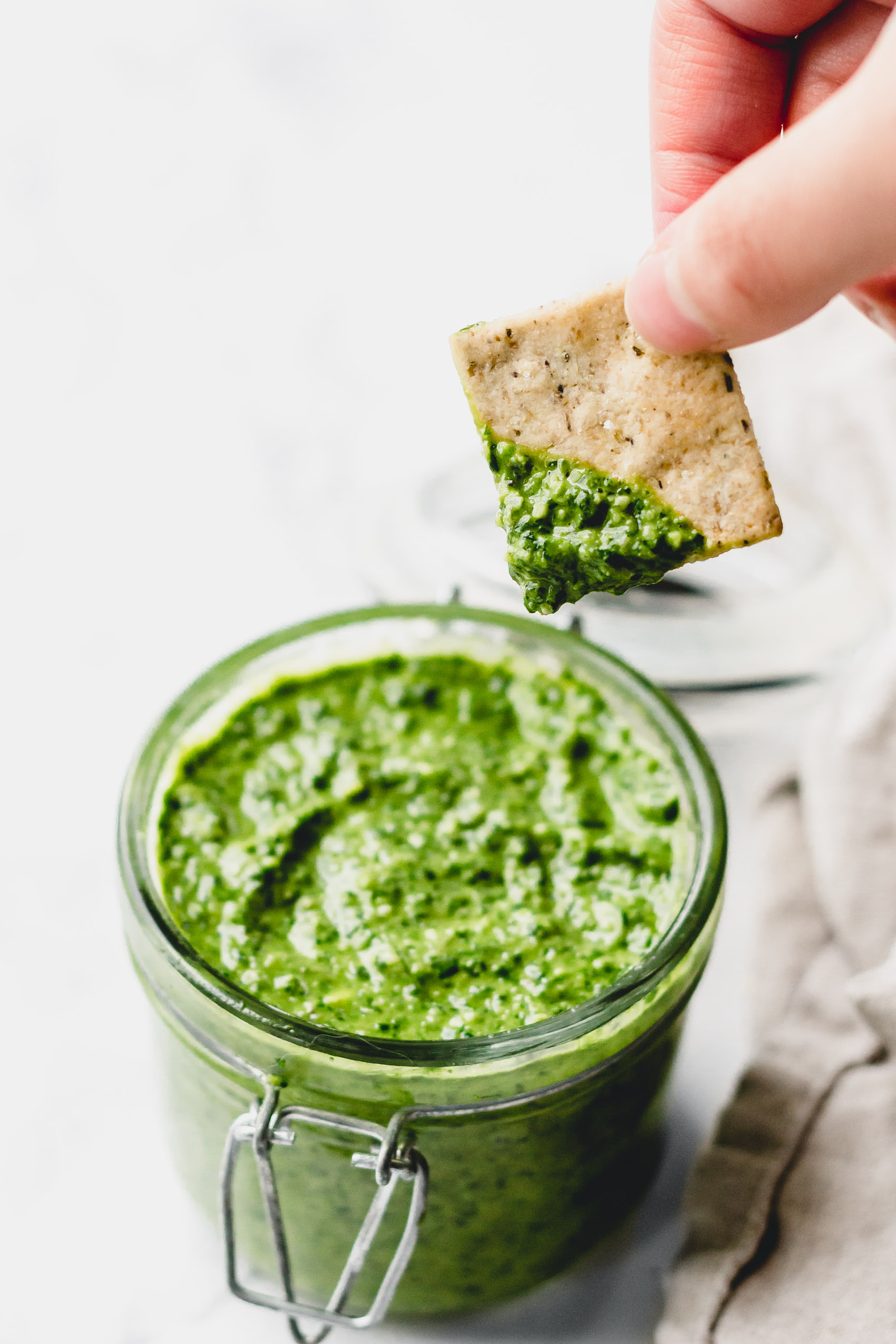 a cracker that has been dipped into a jar of pesto