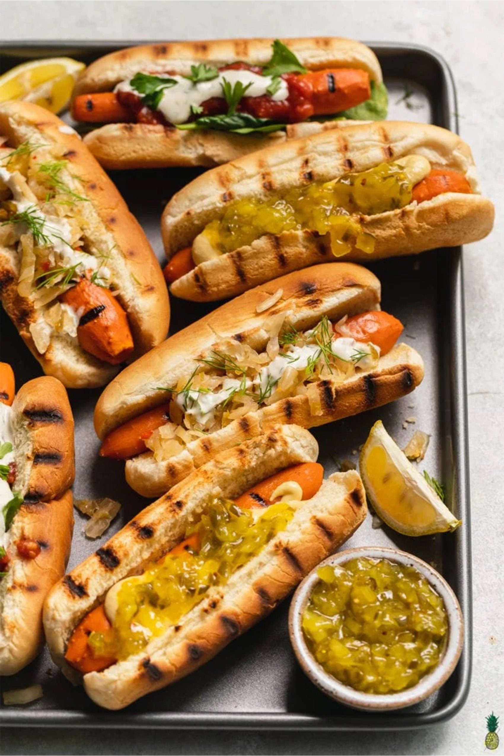 a tray of vegan hot dogs topped with onions and served with lemon wedges