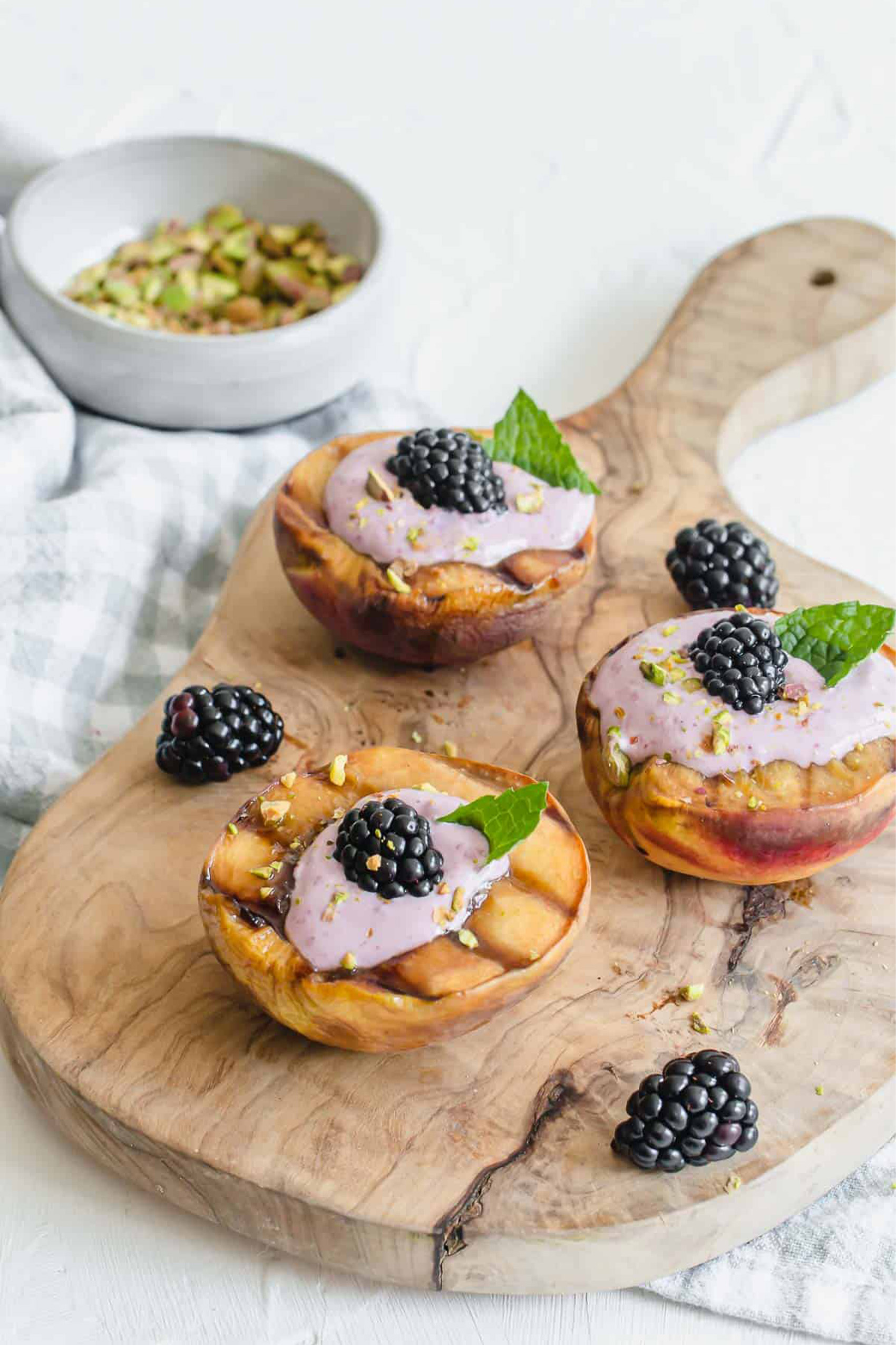 a serving platter of grilled peaches topped with blackberry cream and pistachios