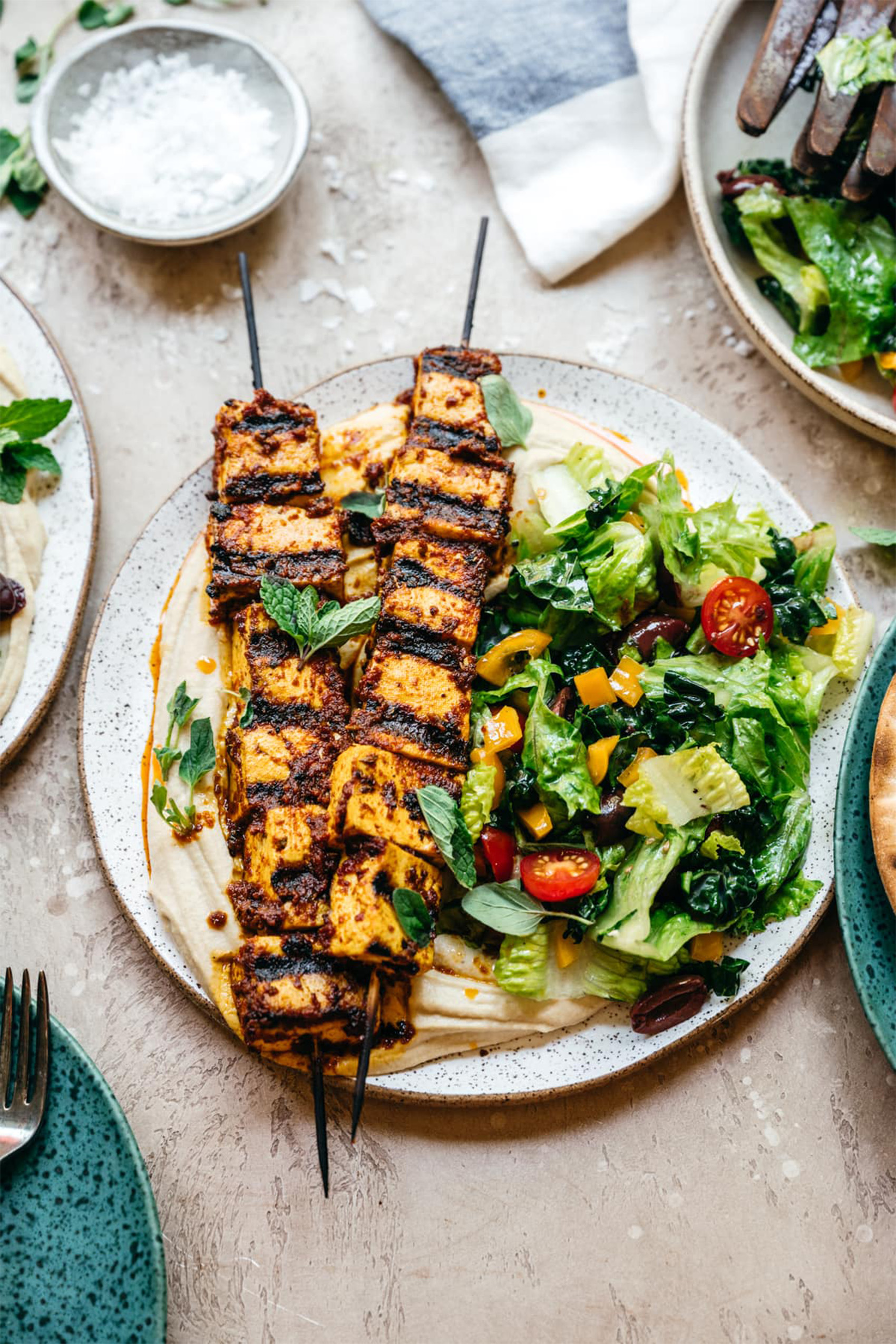 a plate of two grilled tofu kebabs served with a side salad