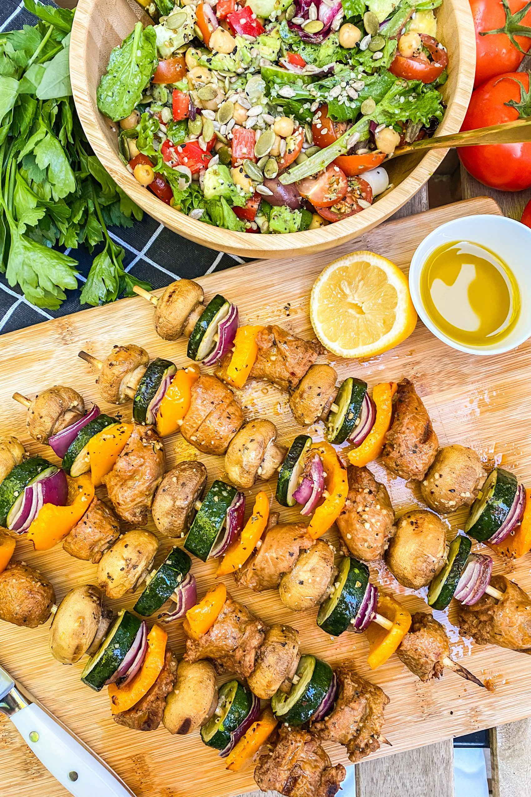 a cutting board holding grilled vegetable skewers served with lemon and dressing