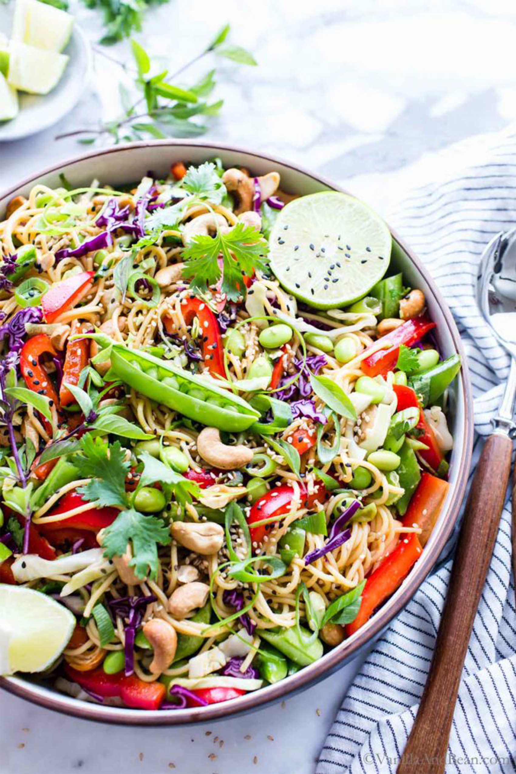 a nowl of pasta served with fresh vegetables, sesame seeds and lime