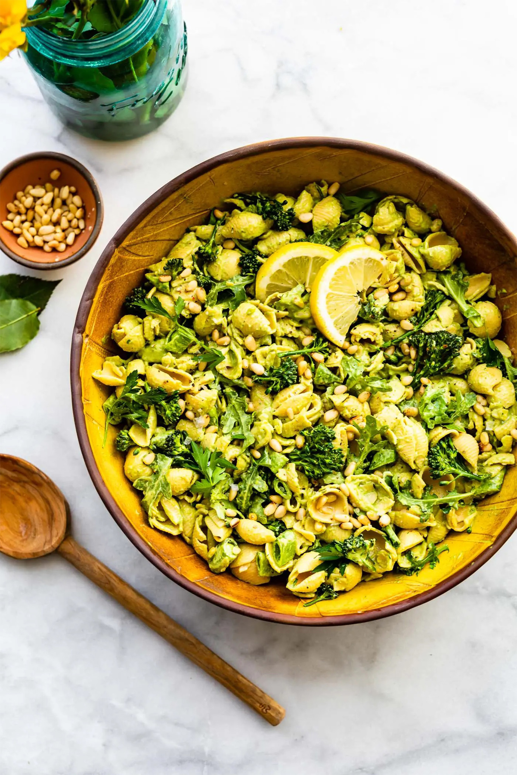 a bowl of vegan green goddess pasta salad served with chili flake, fresh basil and lemon wedges
