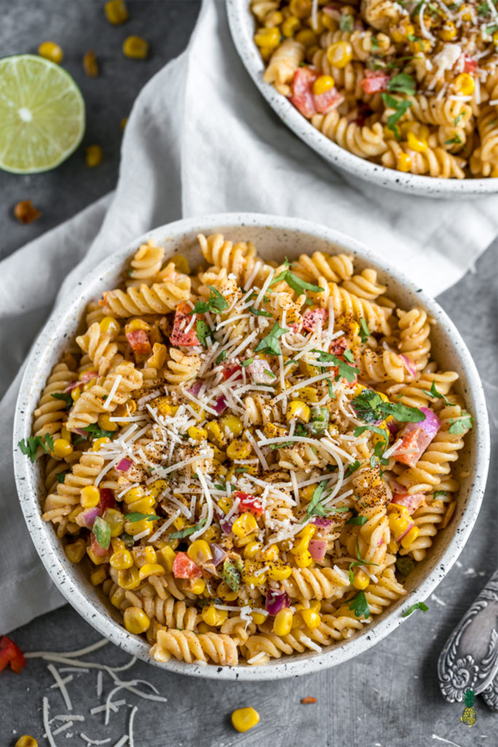 a bowl of fusilli pasta topped with vegan cheese, vegetables and fresh chopped herbs