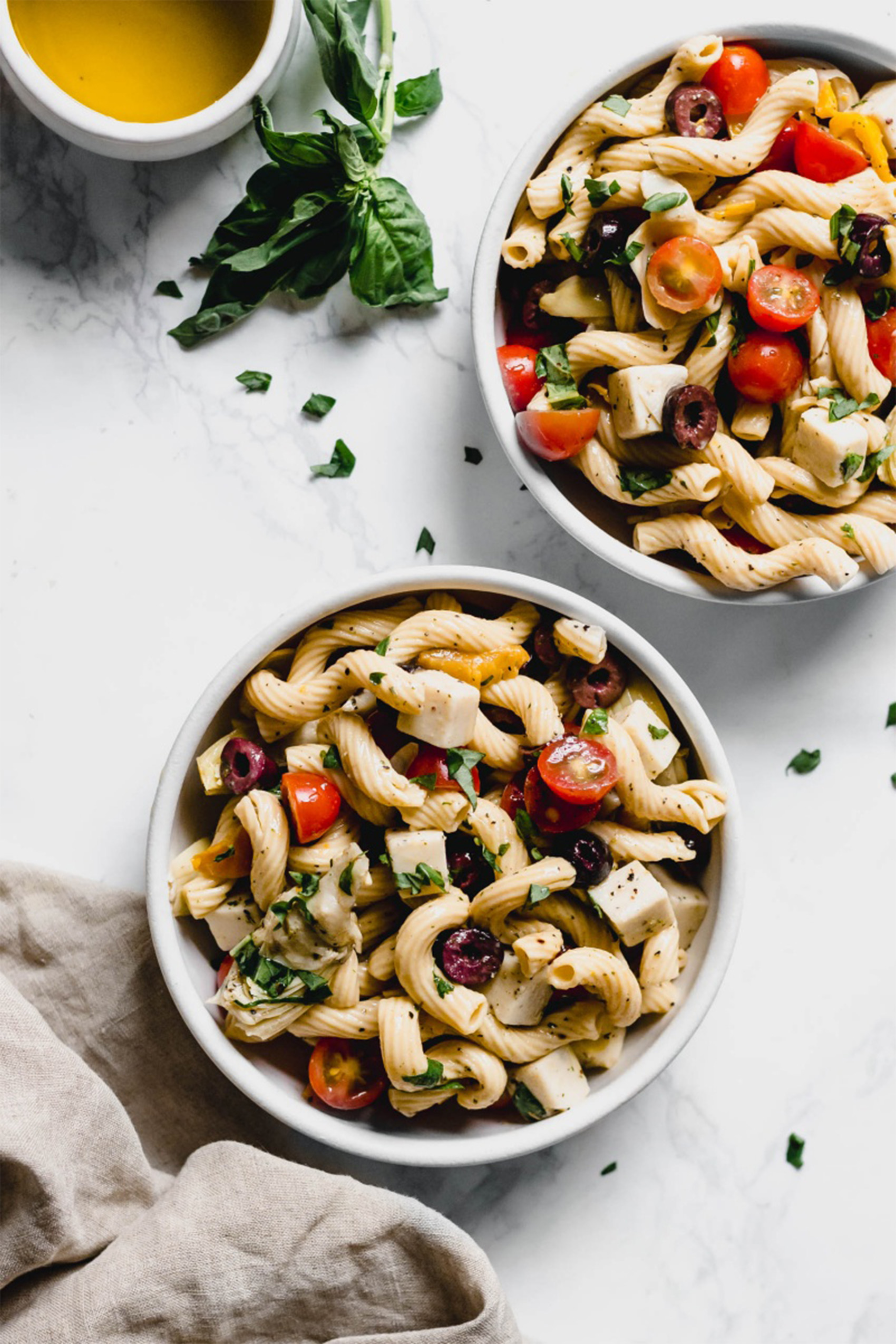 two bowls of italian pasta salad served with fresh basil and olive oil