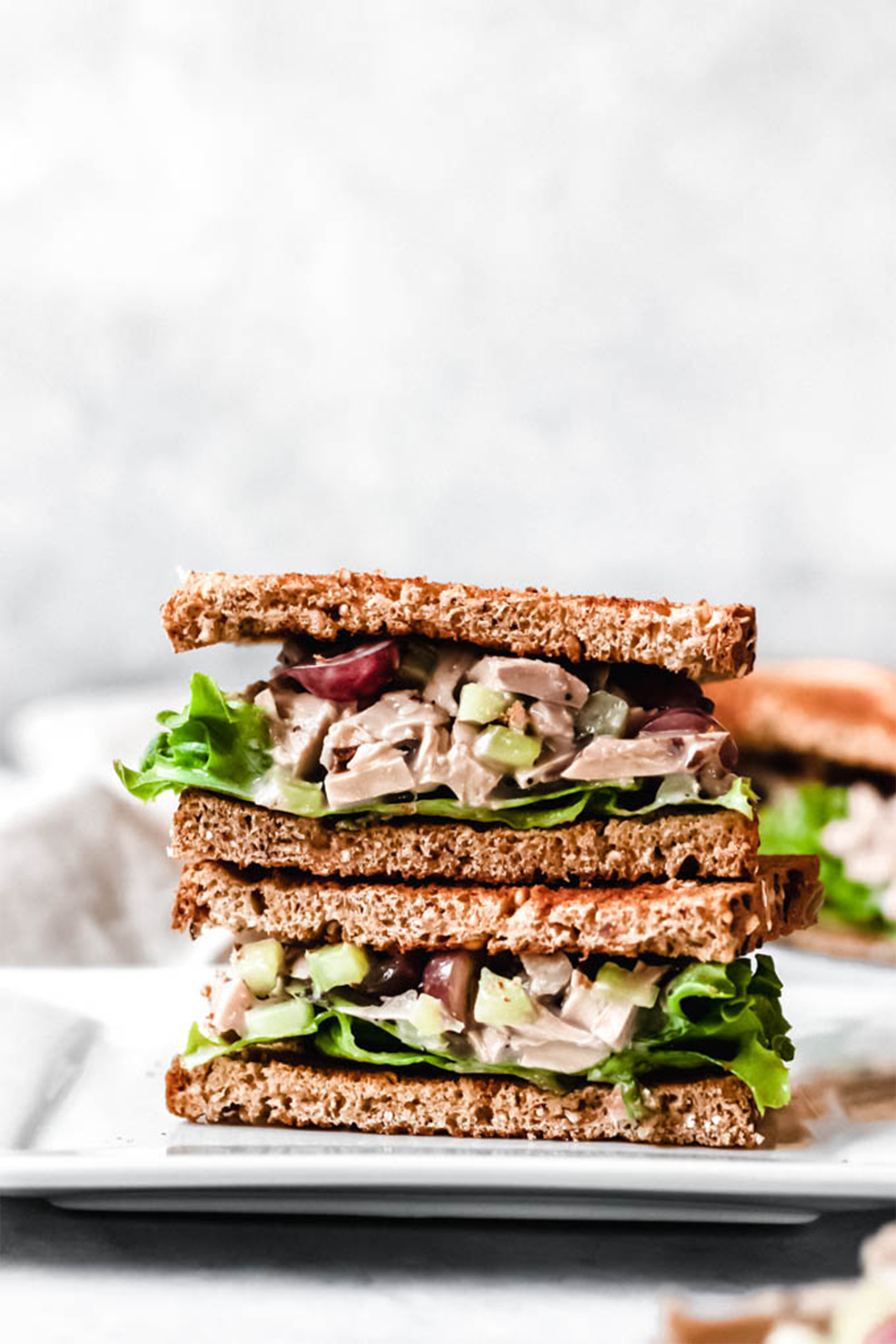 a halved vegan chicken salad sandwich stacked on a white plate