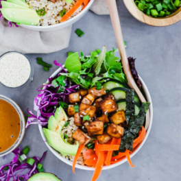 a bowl of greens topped with cucumber, carrots, avocado, cabbage and roasted tofu