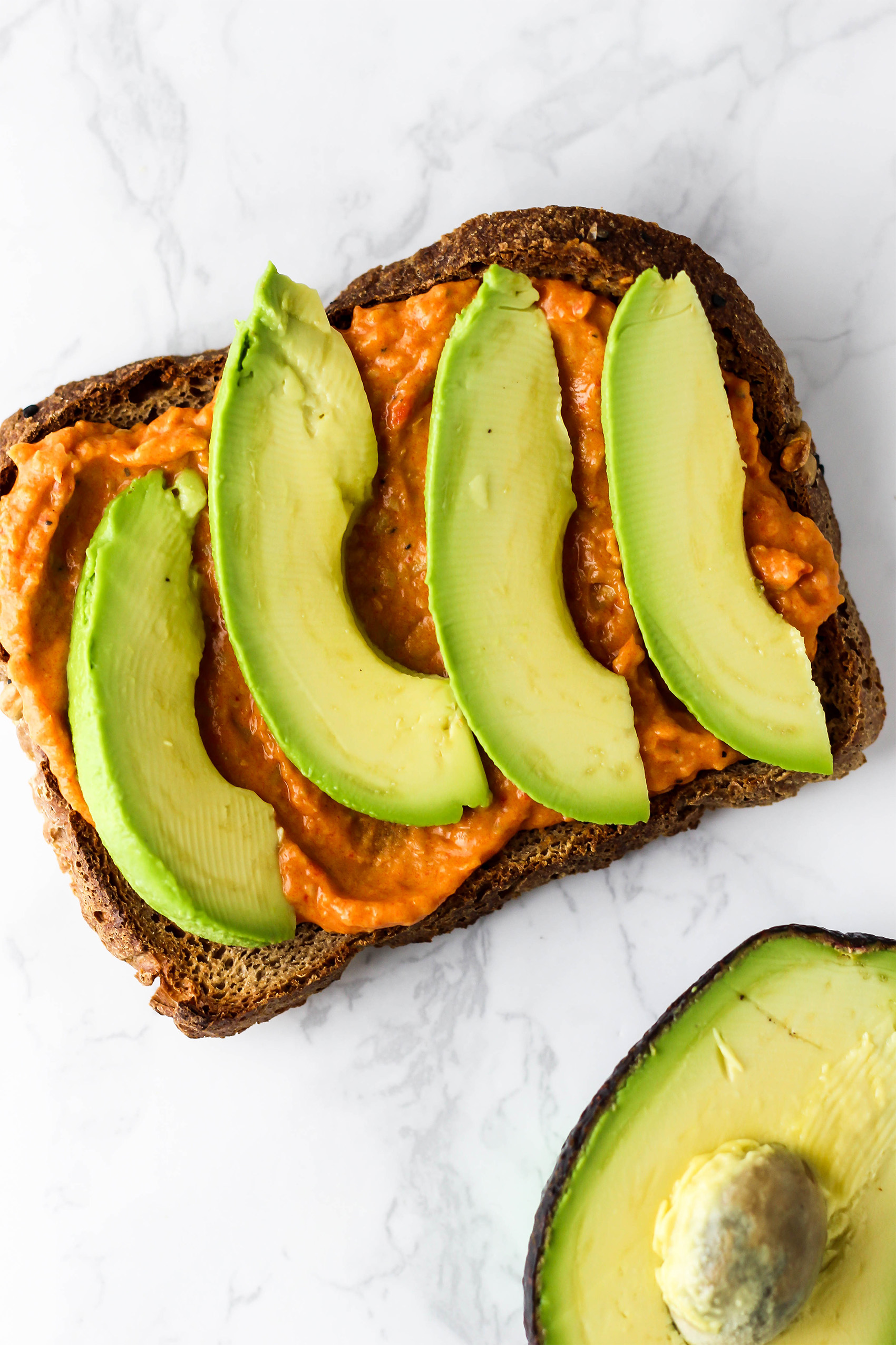 a slice of toast topped with hummus and four slices of avocado