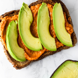 a smear of hummus and sliced avocado served on a piece of toast