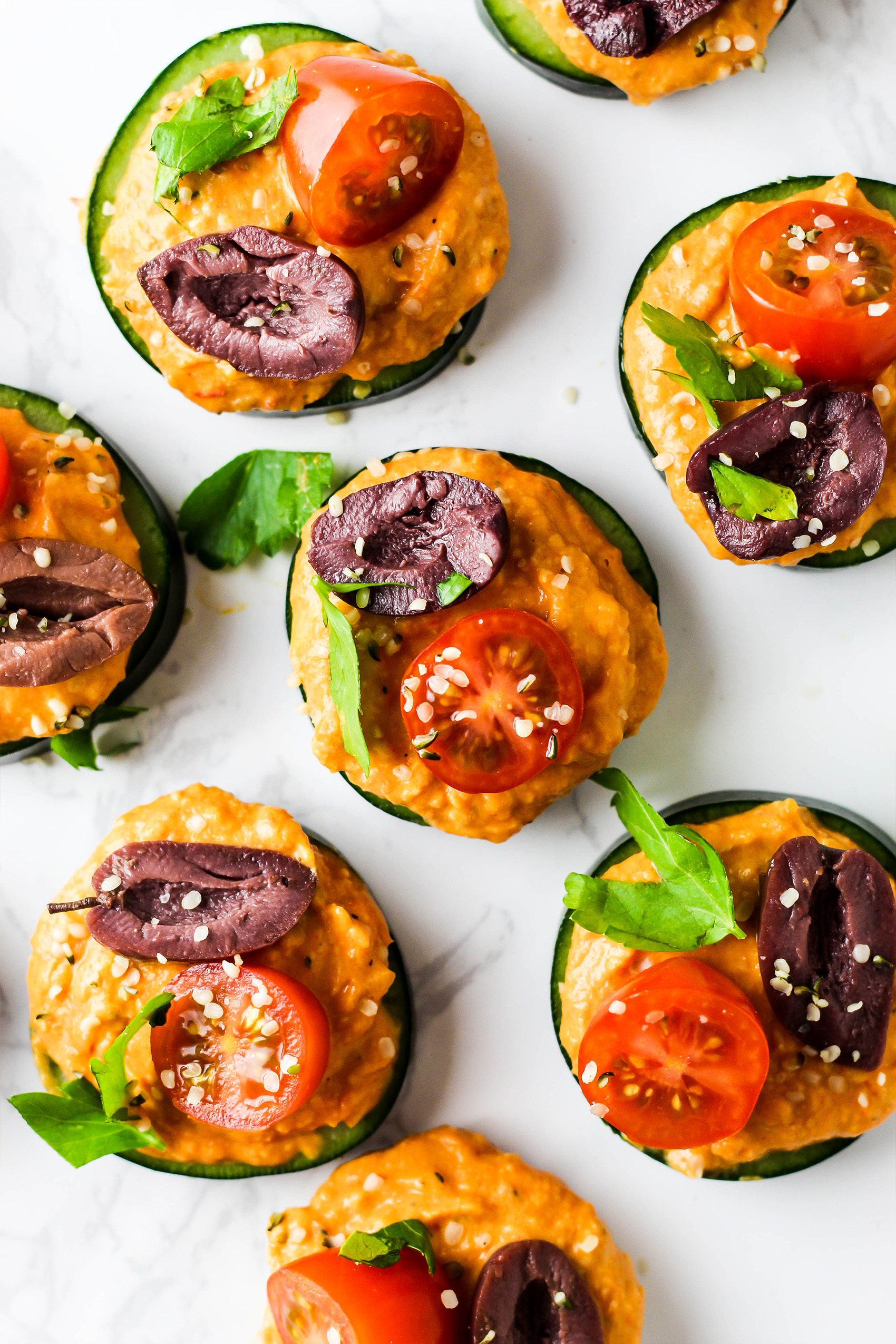 slices of cucumber topped with hummus, tomatoes and olives