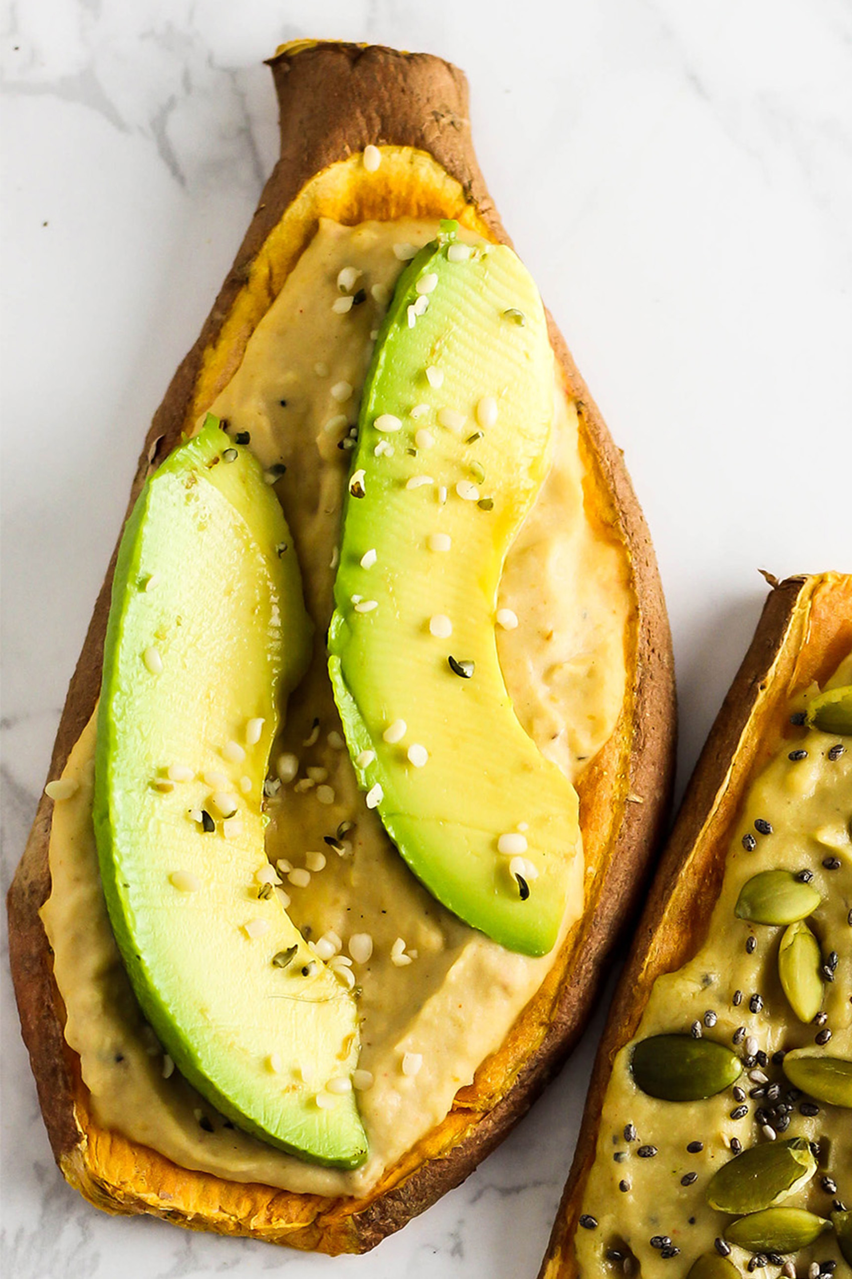 a sliced sweet potato topped with hummus, avocado and hemp seeds