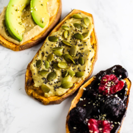 three slices of toasted sweet potatoes, each topped with a different flavor of hummus and various toppings such as seeds and avocado