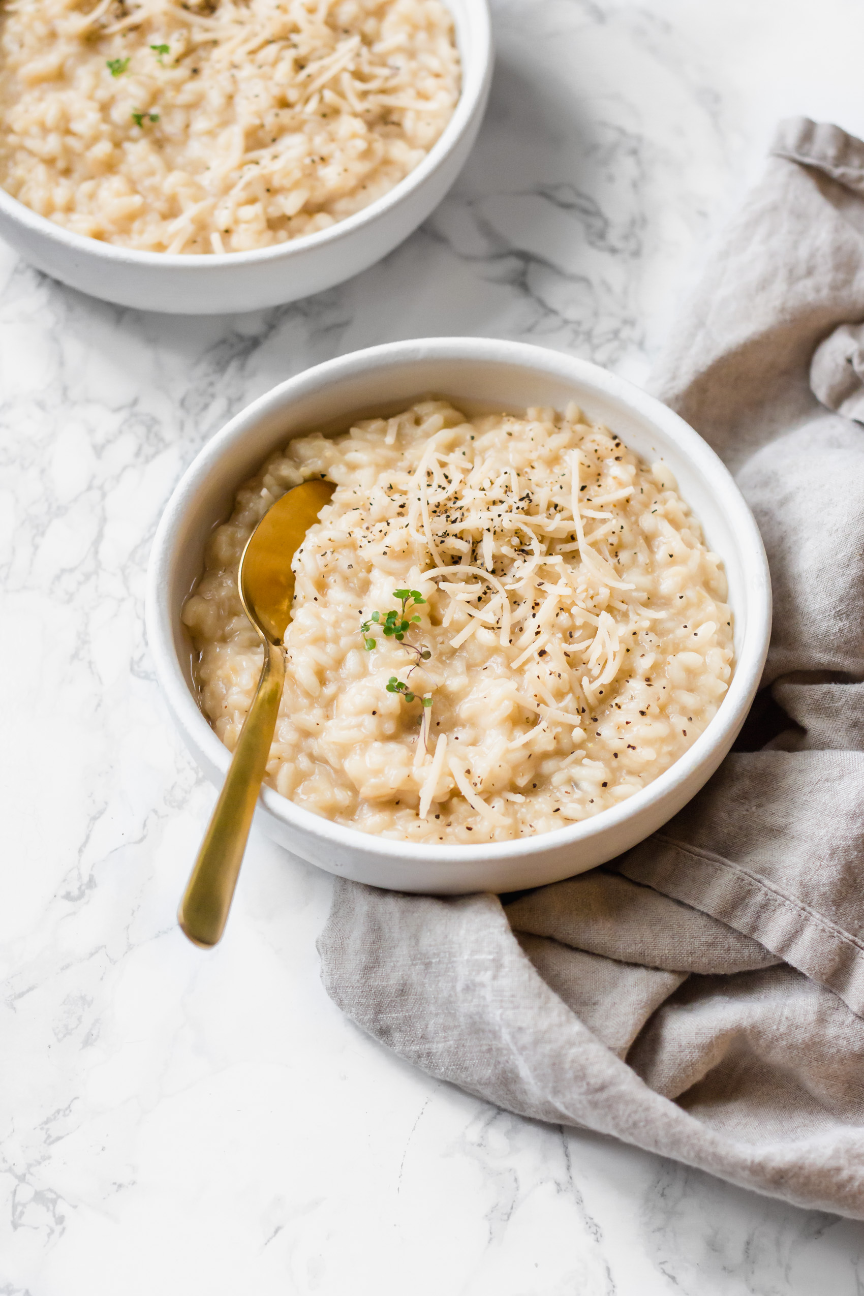 two bowls of creamy vegan risotto, each topped with thyme, cracked black pepper and vegan cheese