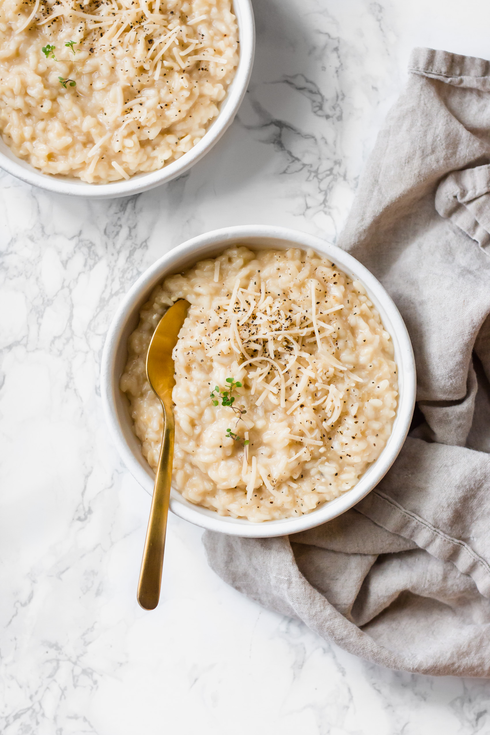 two bowls of vegan risotto topped with dairy-free parmesan shreds, fresh thyme and cracked black pepper