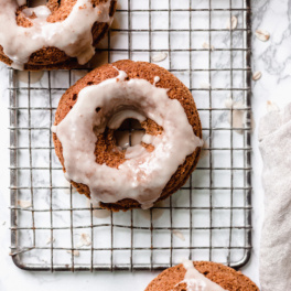 a maple glazed cinnamon donut resting on a cooling rack next to two other donuts