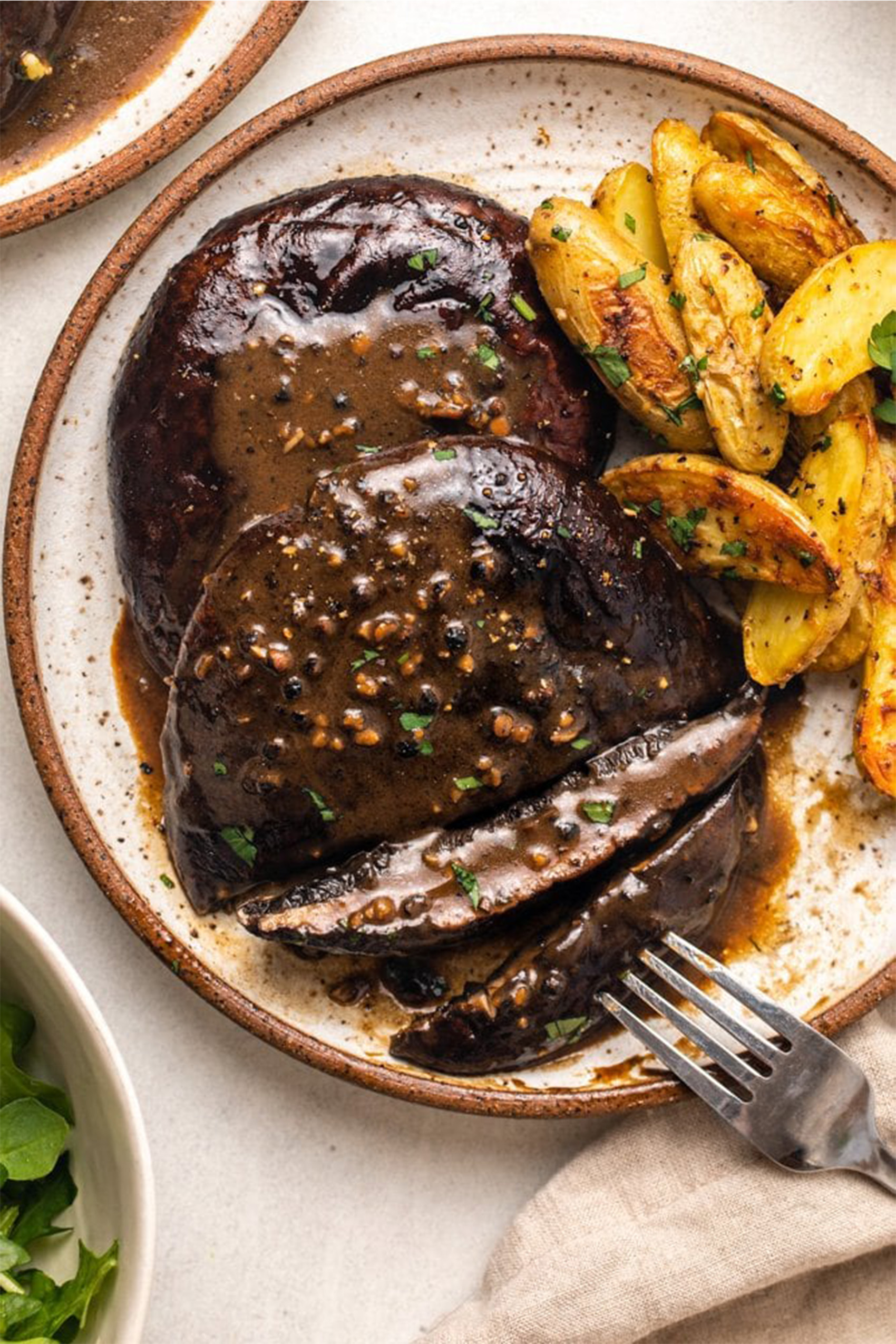 a grilled portobello mushroom served with potatoes and a peppercorn sauce