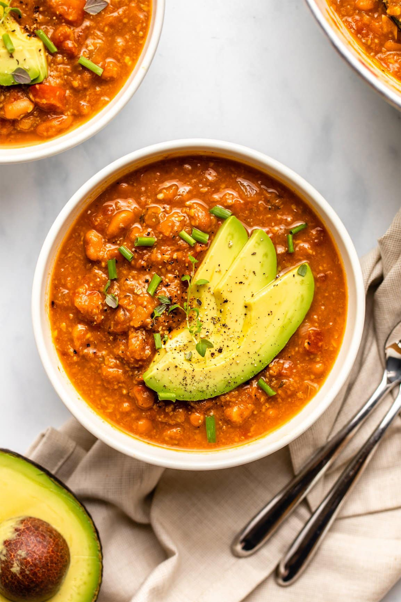 a close up of a bowl of veggie chili topped with sliced avocado