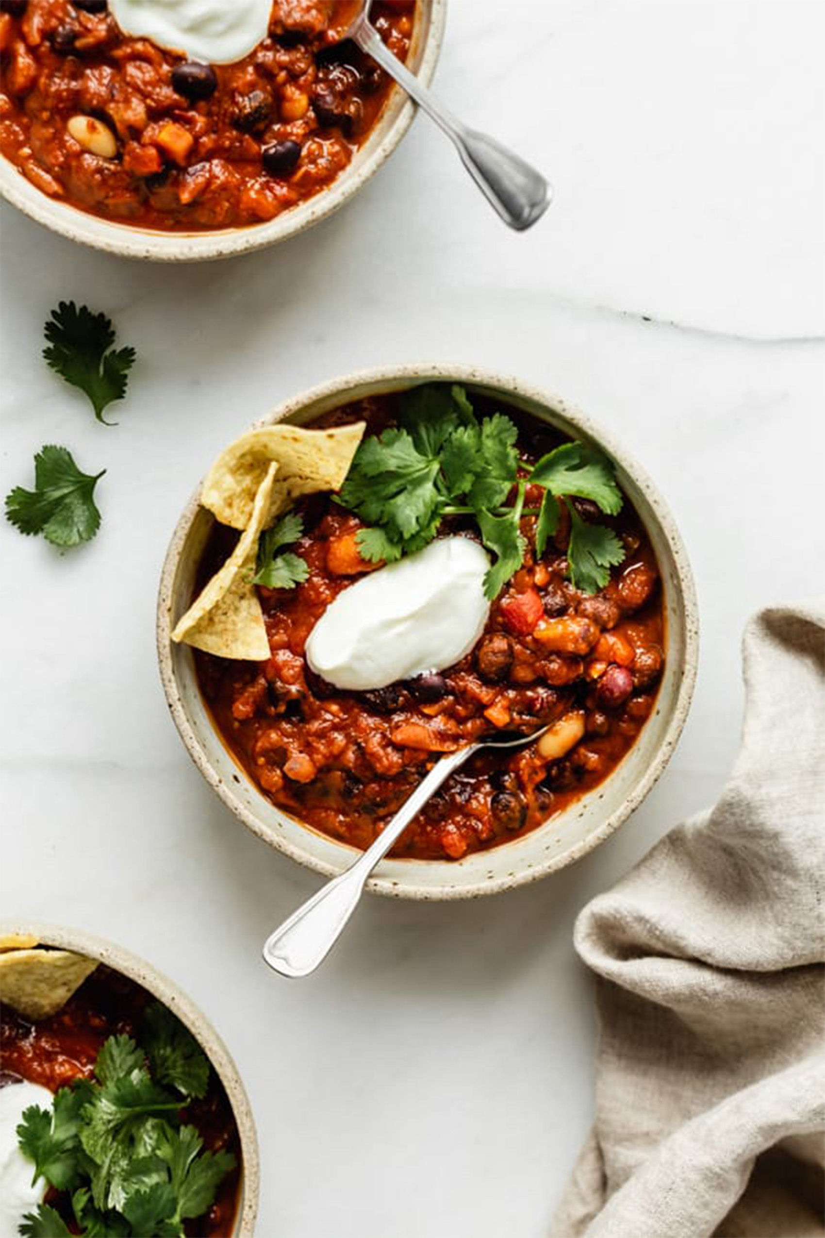 a bowl of vegetarian chili served with tortilla chips, sour cream and herbs