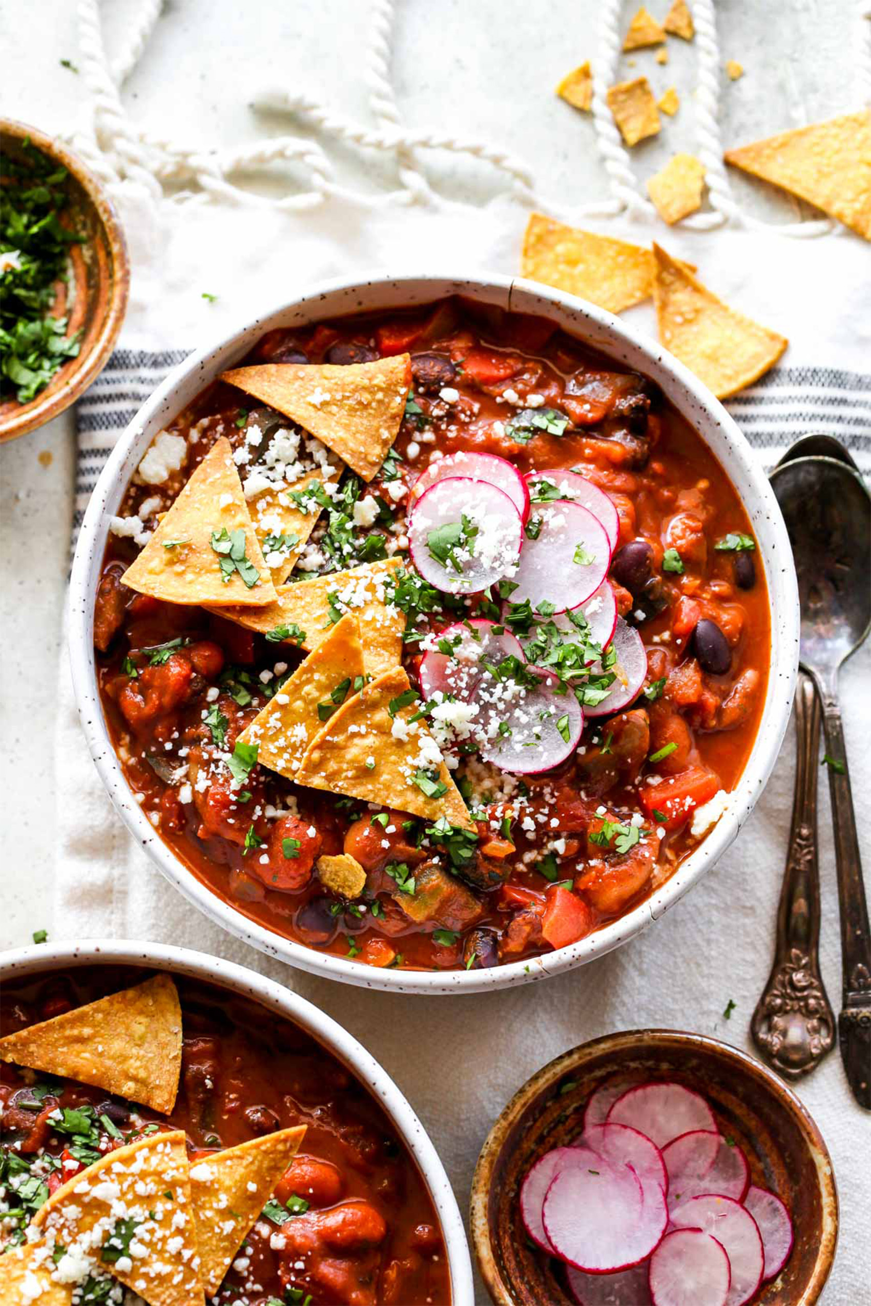 a bowl of vegan chili topped with tortilla chips and sliced radishes