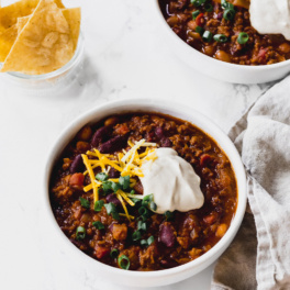 two bowls of vegetarian chili, each topped with herbs, vegan cheese and vegan sour cream