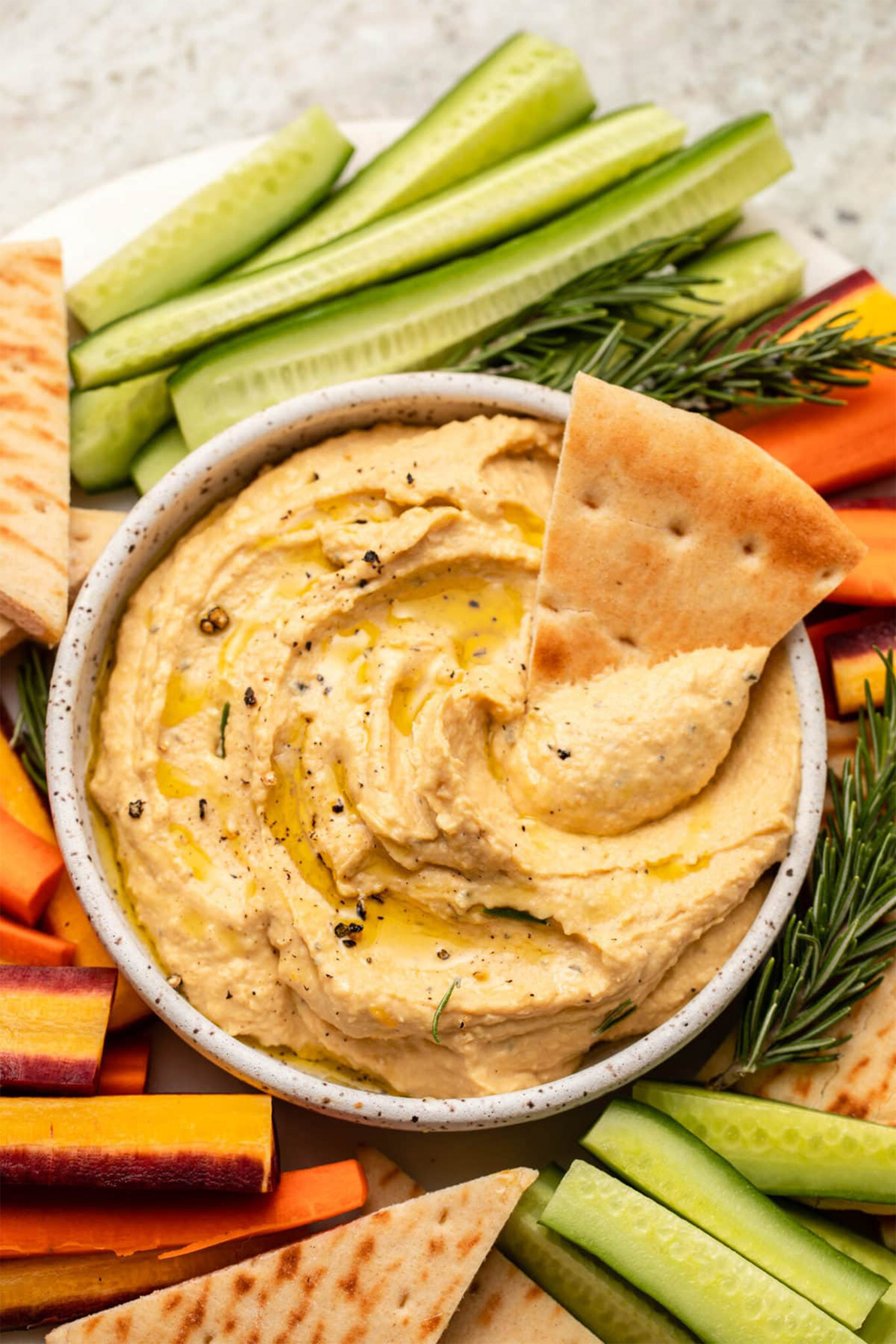 a bowl of butternut squash hummus served with sliced vegetables and pita