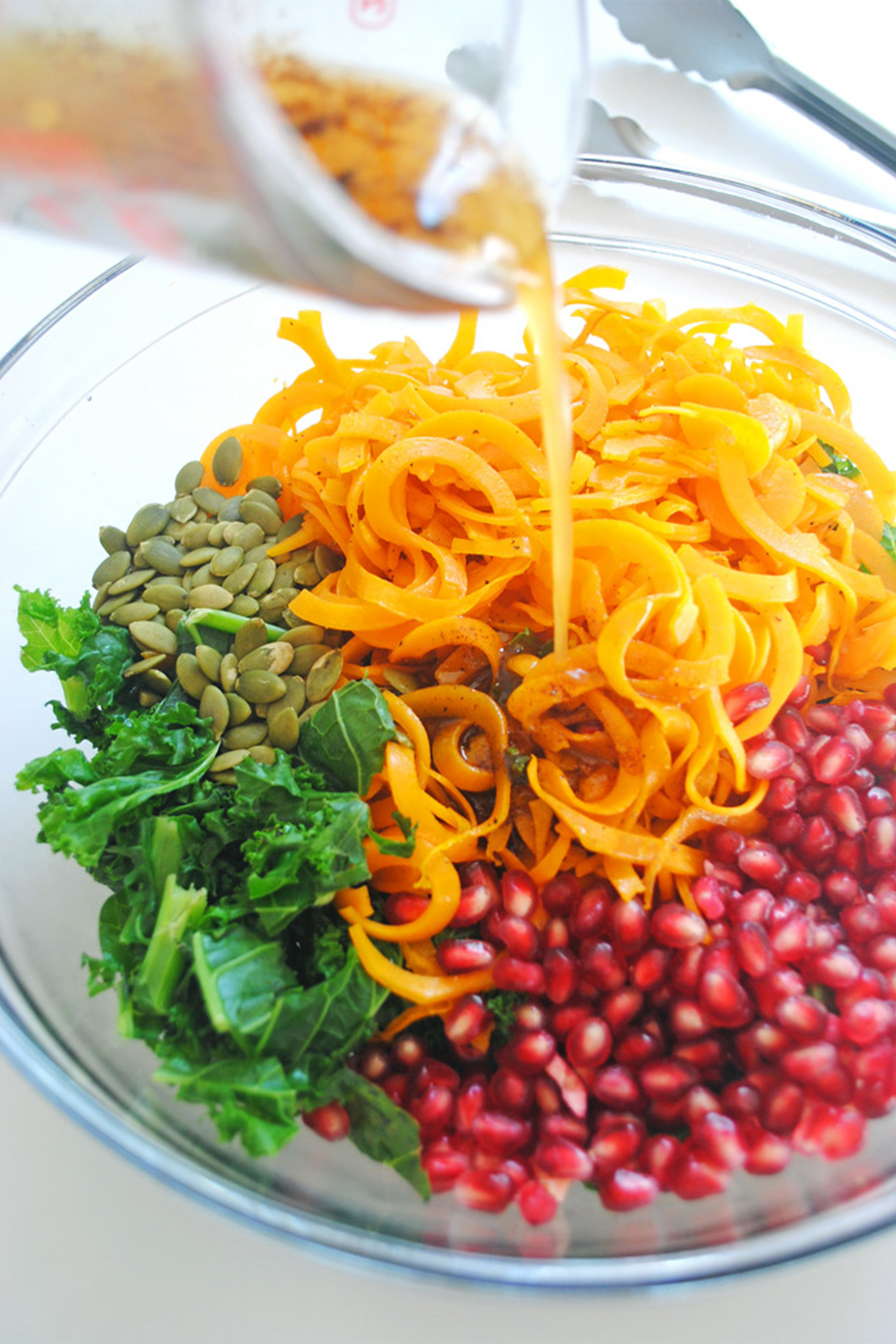 a bowl of spiralized butternut squash with pomegranate, pumpkin seeds and kale