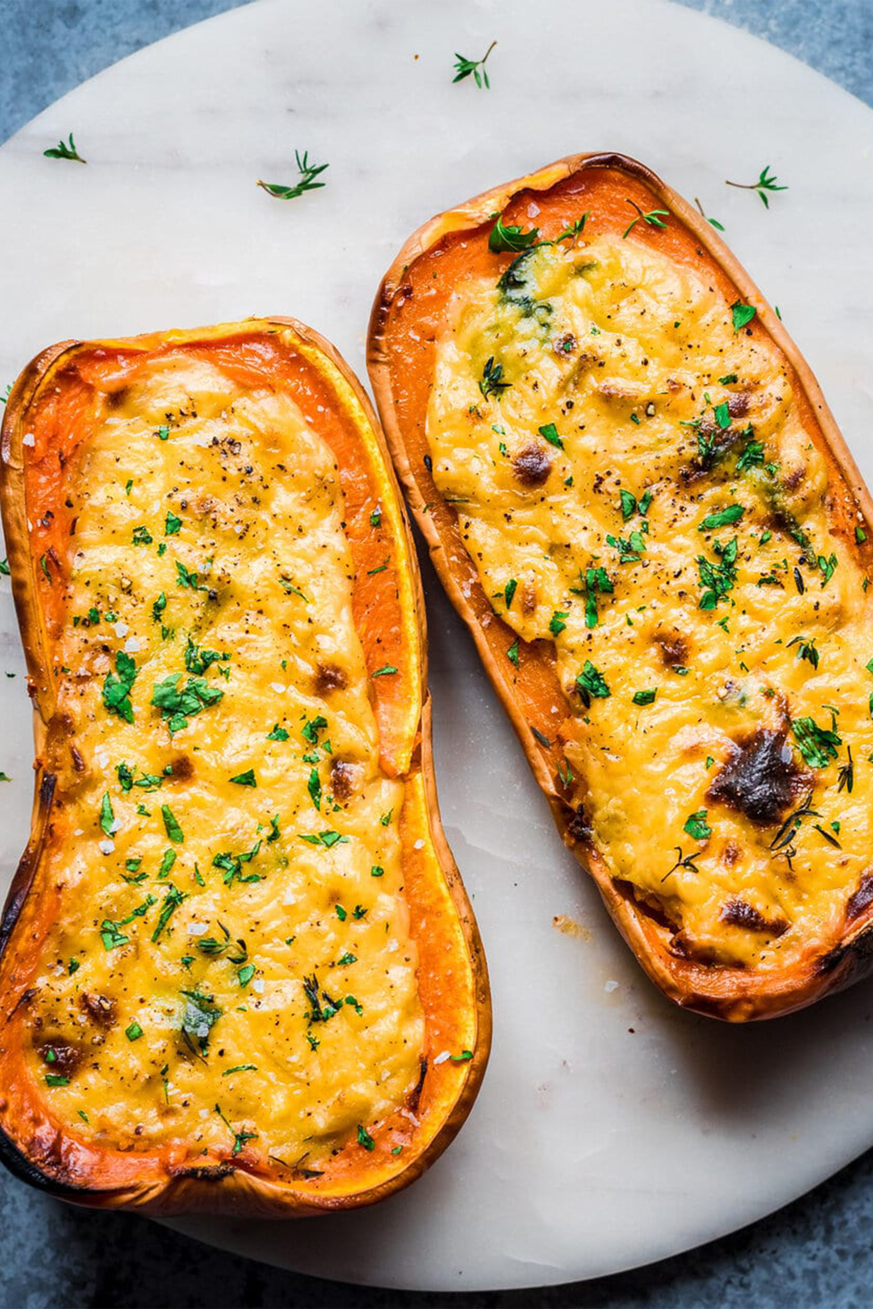 two halves of a butternut squash topped with melted vegan cheese