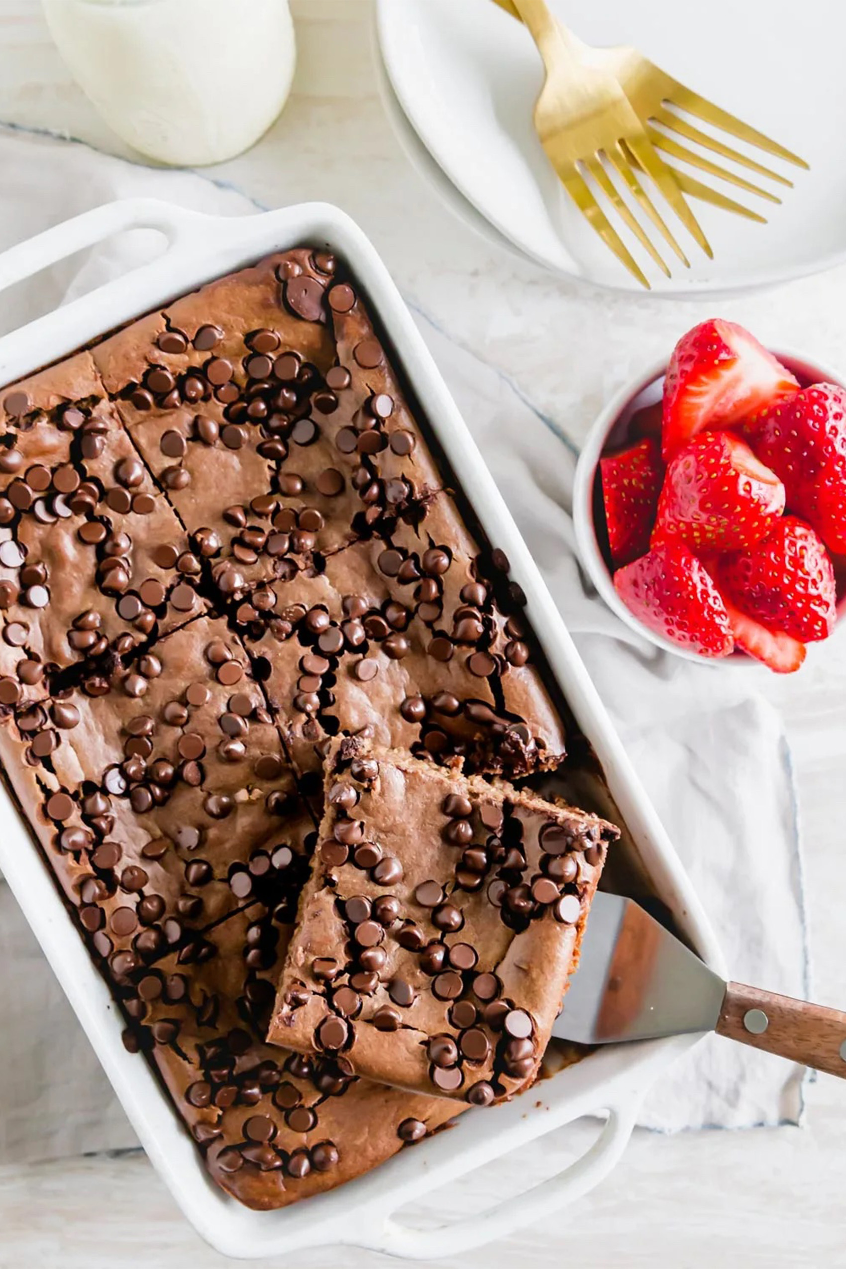 a slice of chocolate baked oats being served from a casserole dish served with a small bowl of halved strawberries