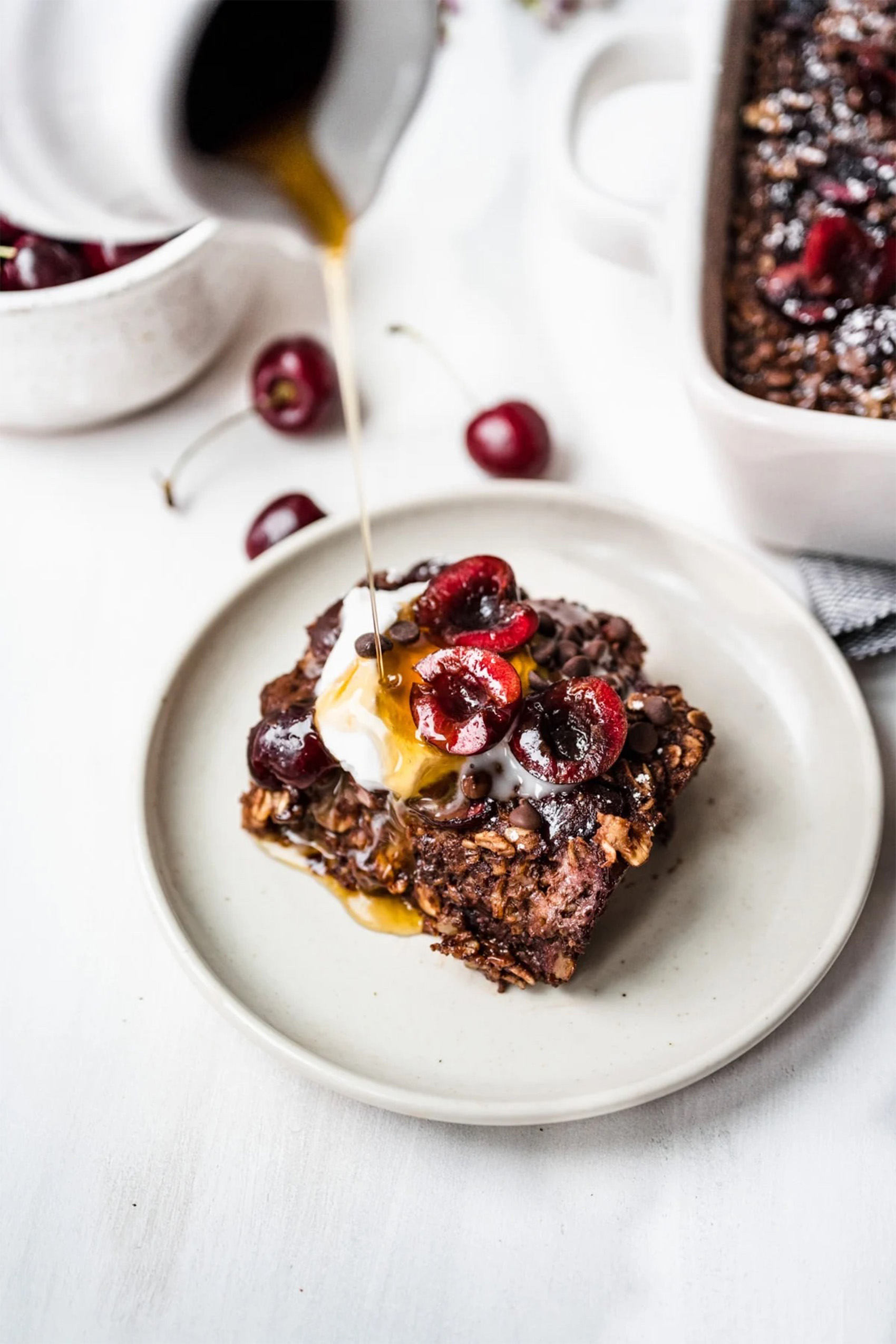 a slice of chocolate cherry baked oatmeal being topped with maple syrup