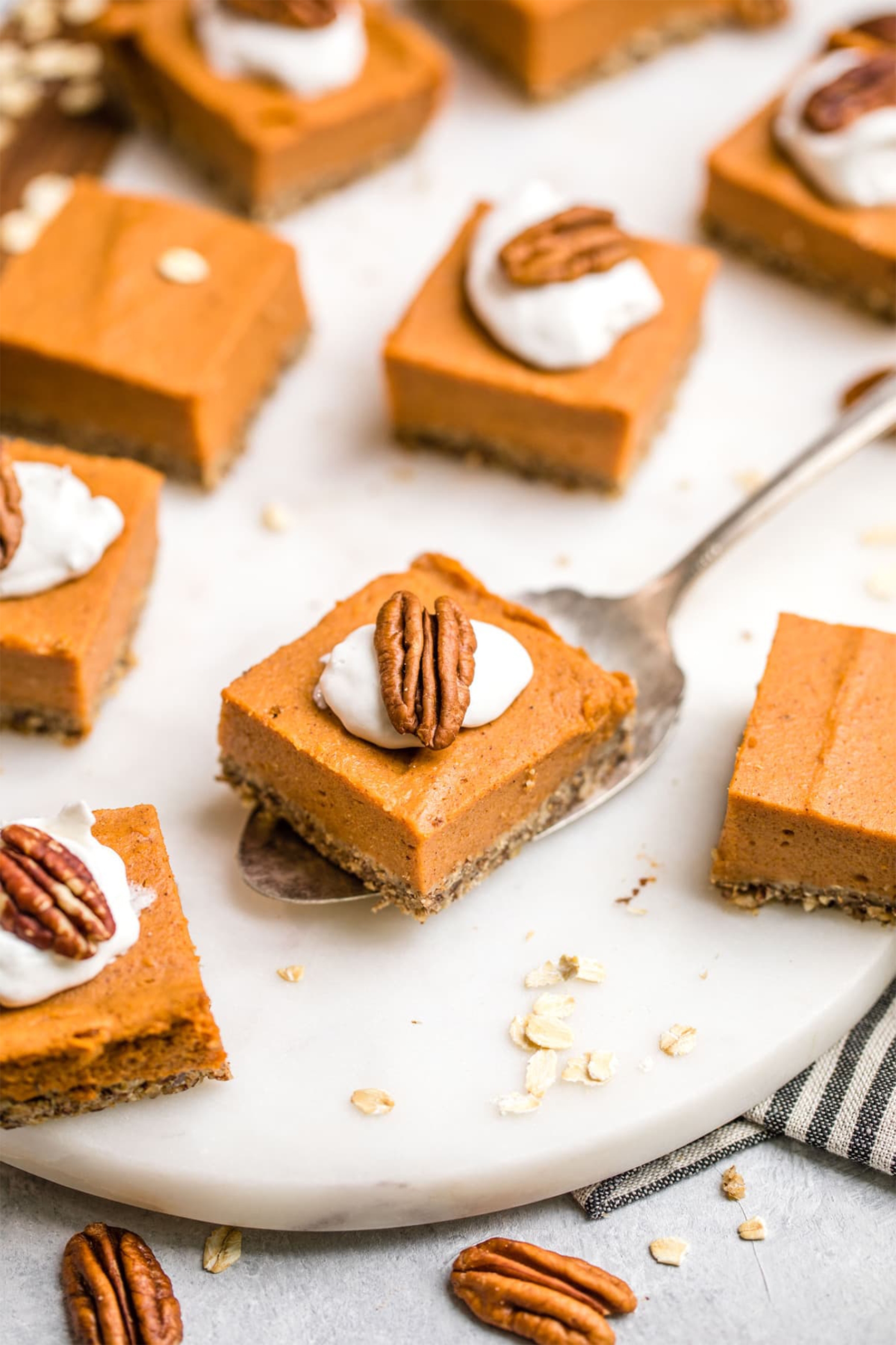 vegan pumpkin pie bars, each topped with whipped cream and a pecan