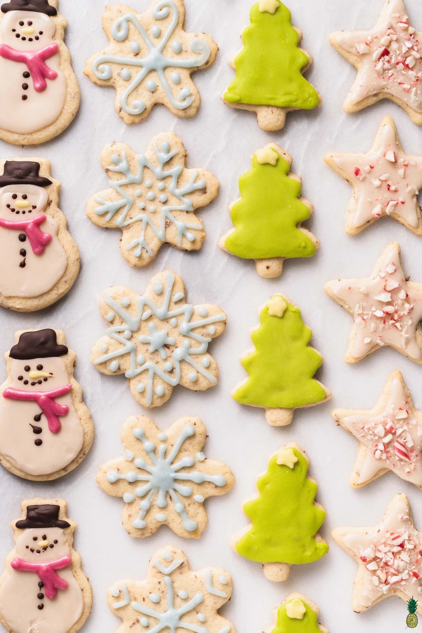 a sheet tray full of vegan sugar cookies shaped like snowmen, snow flakes, christmas trees and stars